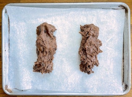 Two logs of biscotti dough on a parchment-lined baking sheet, showing generous spacing between them.